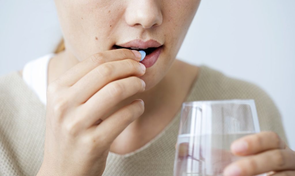A woman places a pill in her mouth while holding a glass of water