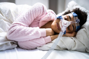 Woman in pink sweater with curly hair sleeping with a cpap mask on.