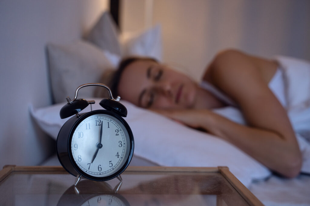 Woman sleeping in bed with a clock on the nightstand