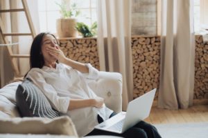 A woman is yawning while trying to work on a laptop