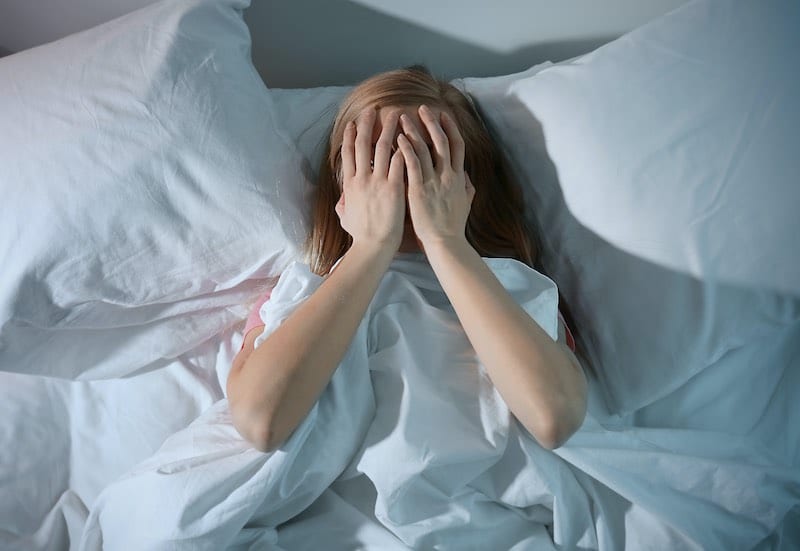 What Causes Restless Sleep? Young woman lying in bed with hands over face
