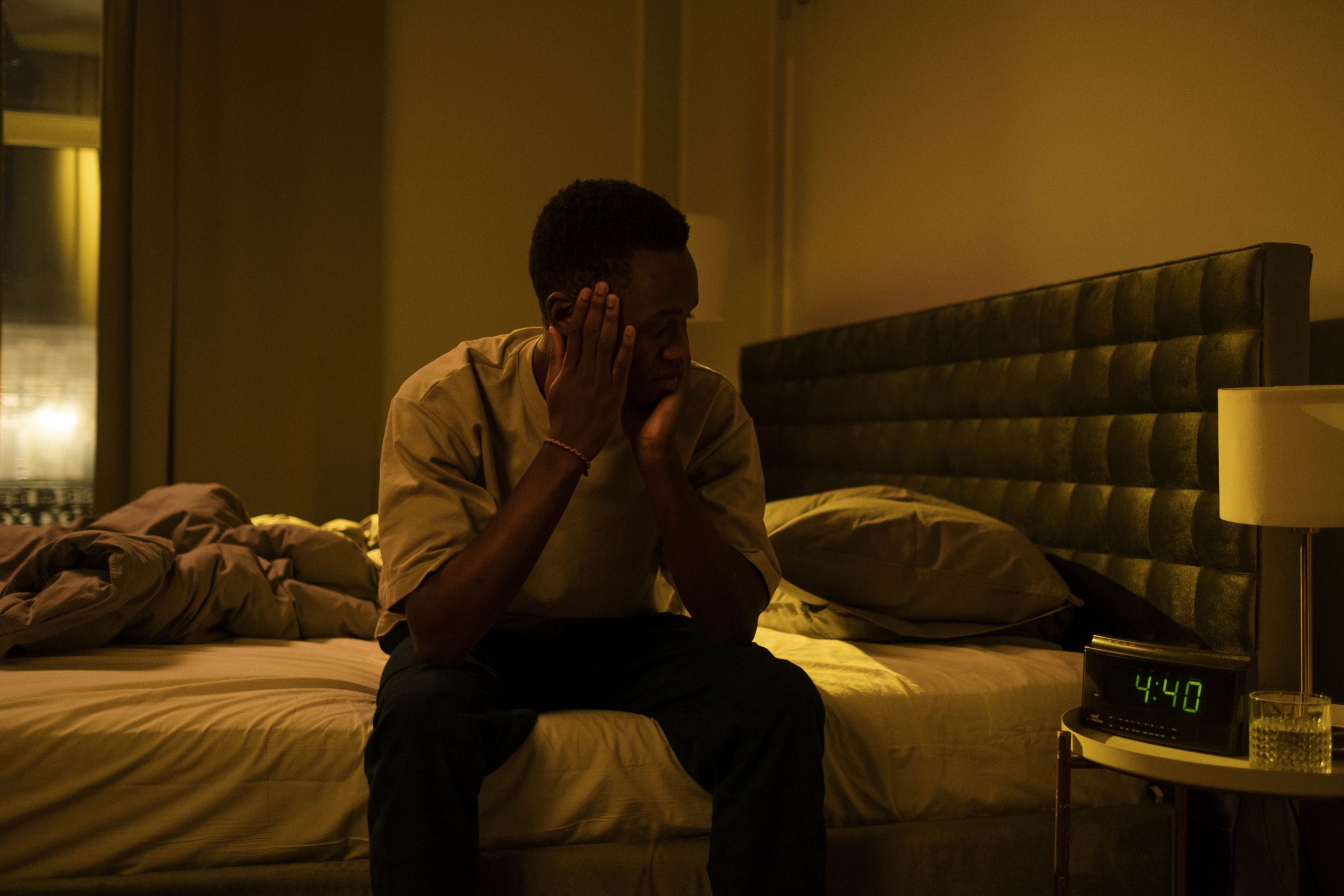 Restless Sleep African American man sitting on a bed struggling with insomnia at night.