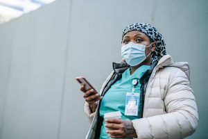 How Is Shift Work Disorder Diagnosed? Nurse wearing mask and uniform using smartphone during outdoor coffee break.
