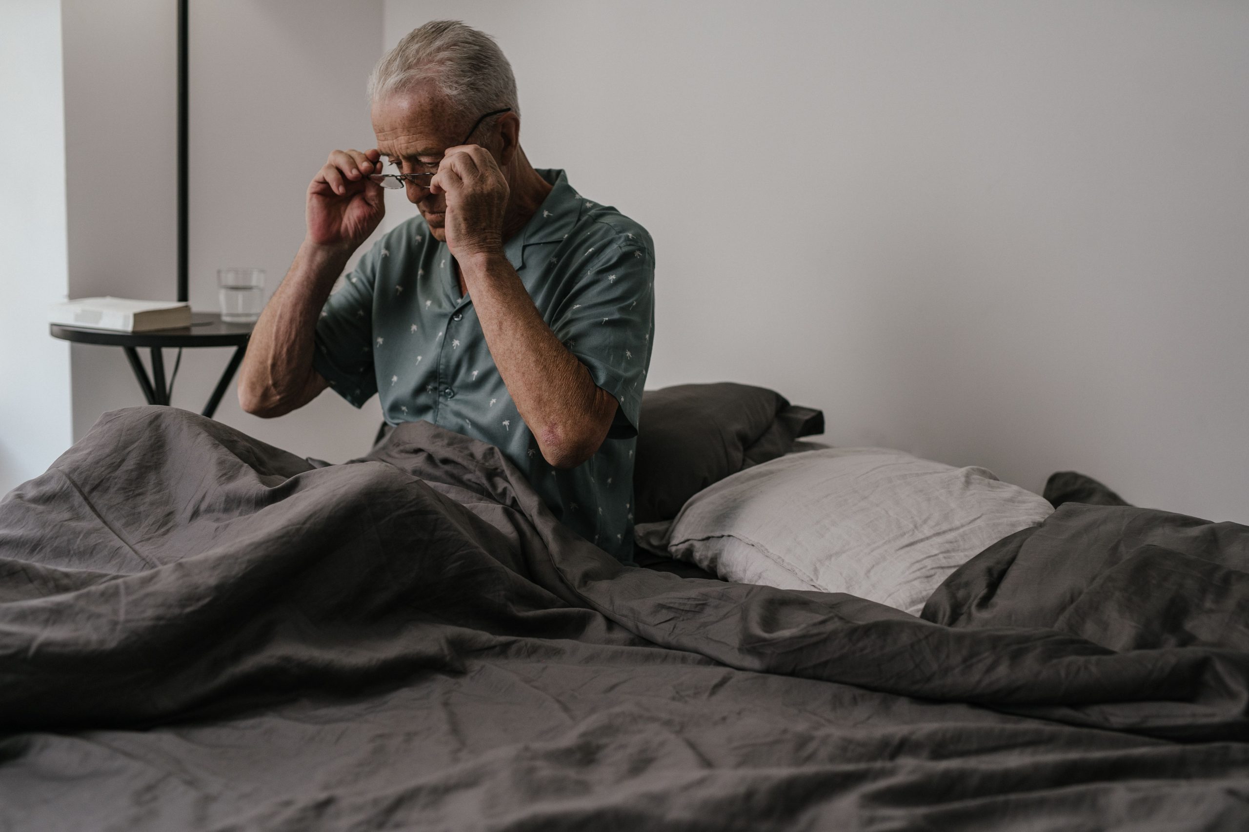 How to Get a Good Night’s Sleep Senior man adjusts glasses while sitting in bed, expressing morning routine and daily life.