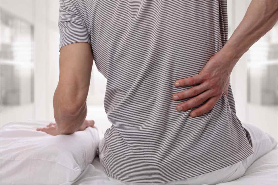 Man sitting on bed grabbing back in pain