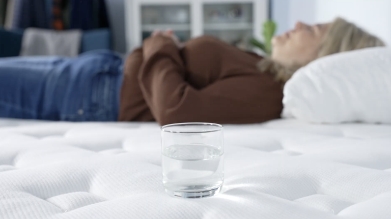 Glass of water on a mattress with a Sleep Foundation tester lying in the background