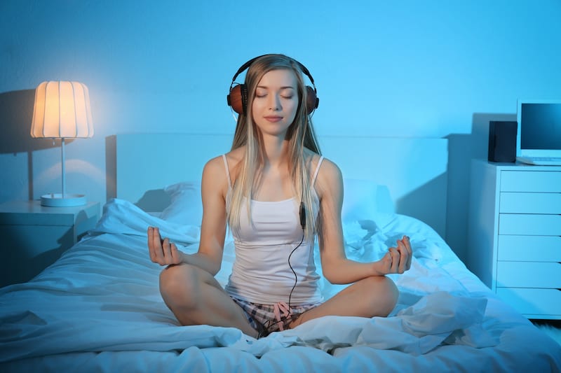 Woman seated in bed in meditation pose with headphones on