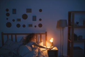 A curly-haired young woman lying in bed and switching off bedside lamp while preparing to sleep