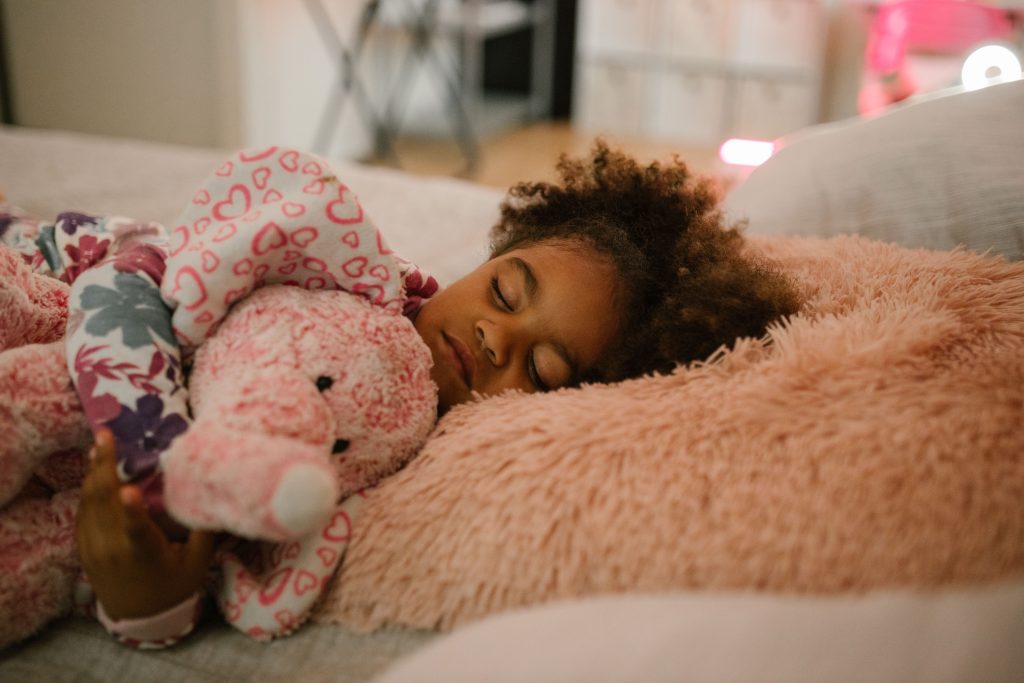 Children and Sleep A young girl sleeping peacefully with a pink stuffed animal in a cozy bedroom environment