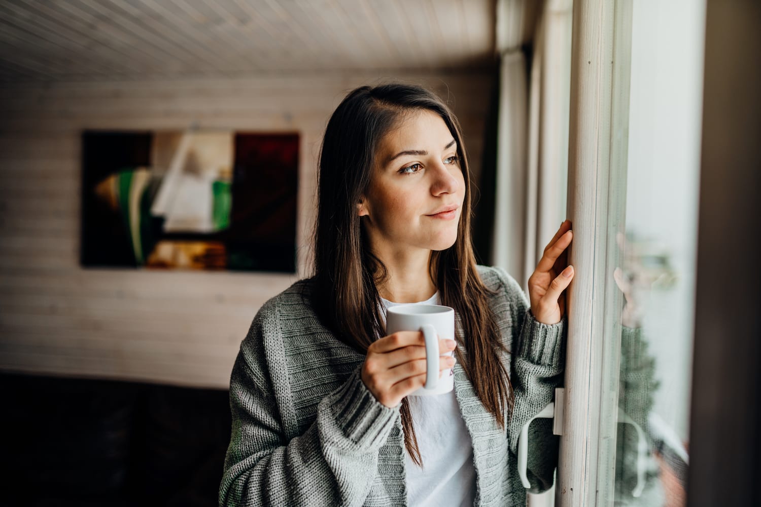 woman looking out window with cup of coffee