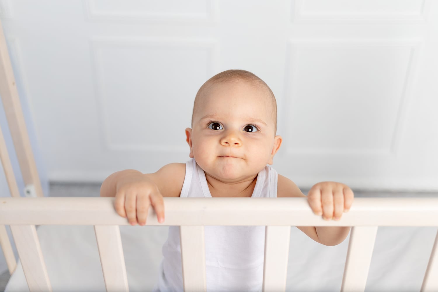 portrait of a smiling baby boy 8 months old standing in a crib