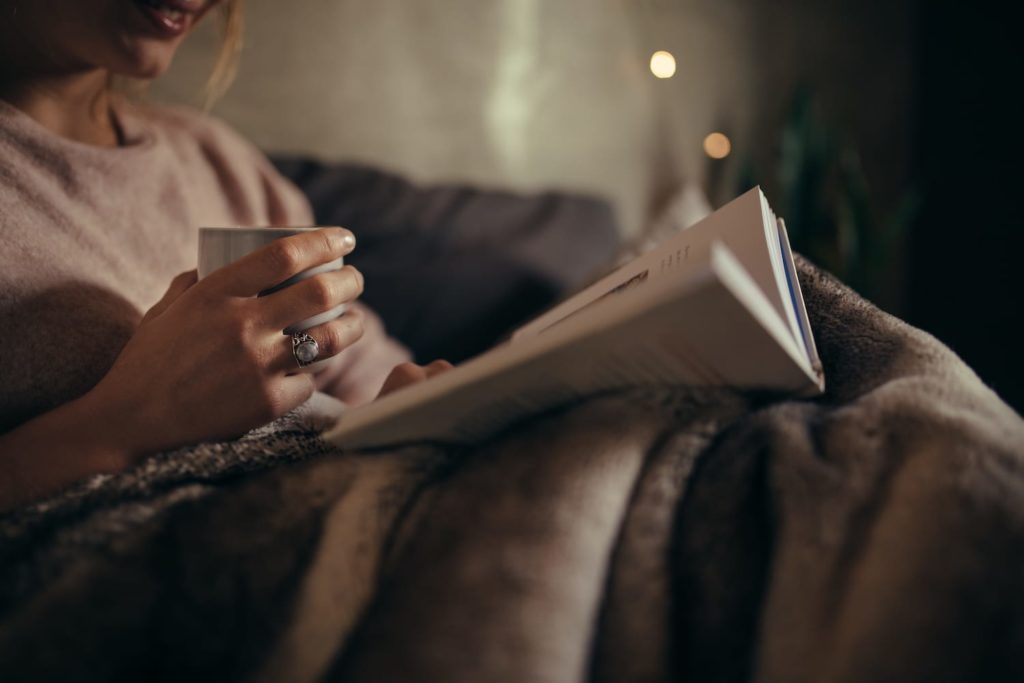 women reading a book with a cup of coffee at night