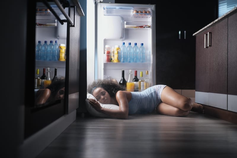 Young woman sleeping on floor in front of open refridgerator