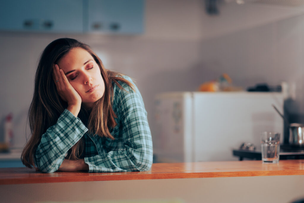 Woman wearing her pajamas falling asleep in the kitchen.