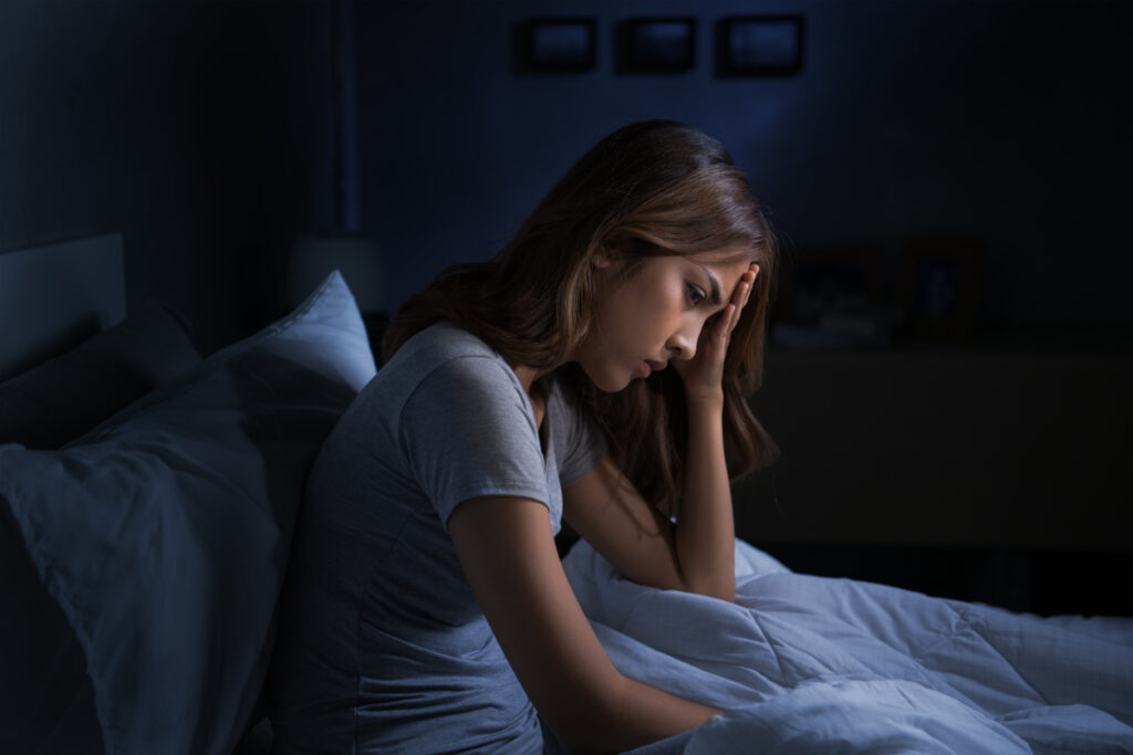 Depressed young woman sitting in bed cannot sleep from bad dreams
