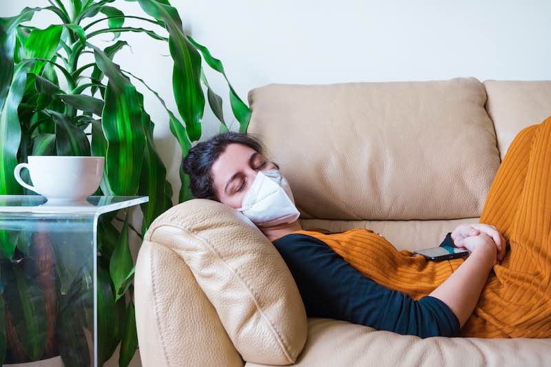 A woman naps on a couch wearing a mask