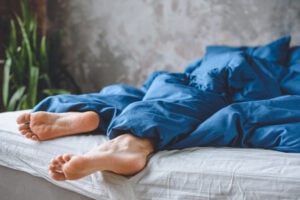 Image of sleeping man's restless legs under blanket in bed at home.