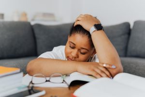 Sleep Deprivation A woman rests on textbooks, exhausted from studying in her cozy living room environment