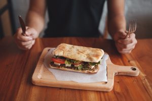Sleep and Overeating Big sandwich close up. Young man holding a fork and knife getting ready to eat healthy greek sandwich. Food at restaurant concept
