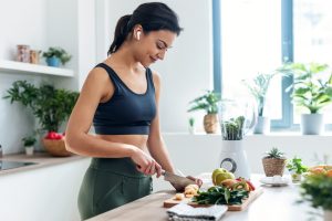 Diet, Exercise, and Sleep Shoot of athletic woman cutting fruits and vegetables to prepare a smoothie while listening to music with earphones in the kitchen at home