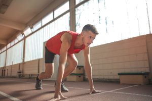 Focused male athlete in starting position indoors, ready to sprint.
