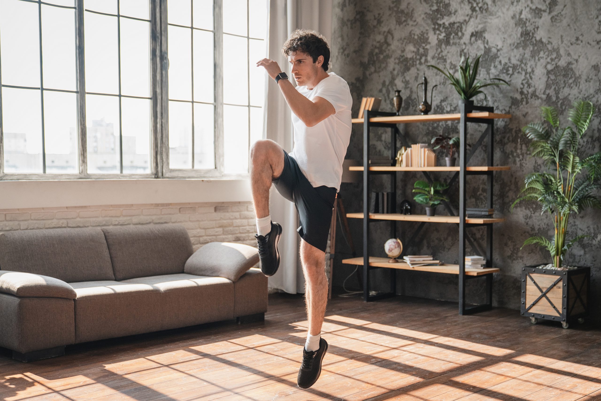 What Is the Best Time to Exercise for Sleep? Young athletic man jumping during home workout, exercising and training indoors. Fitness routine, active lifestyle, healthy body care and sports concept in living room.
