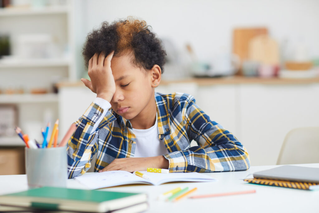 A tired boy falling asleep at desk while doing homework.