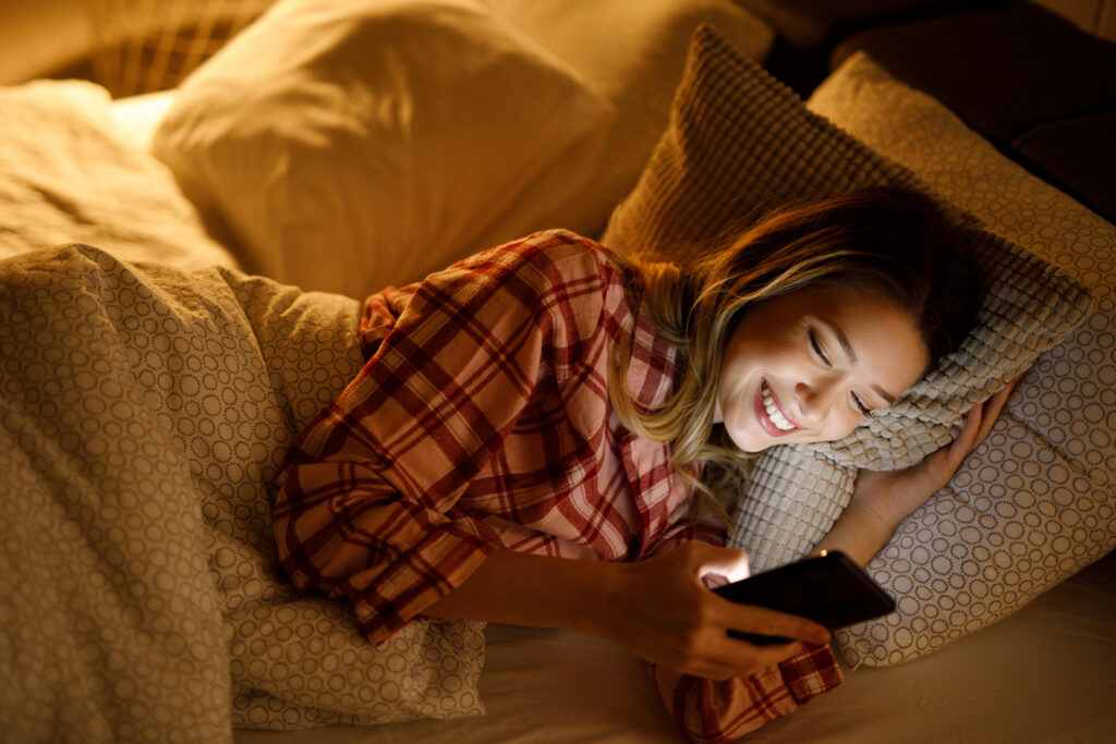 A young woman using a mobile phone in bed late at night.