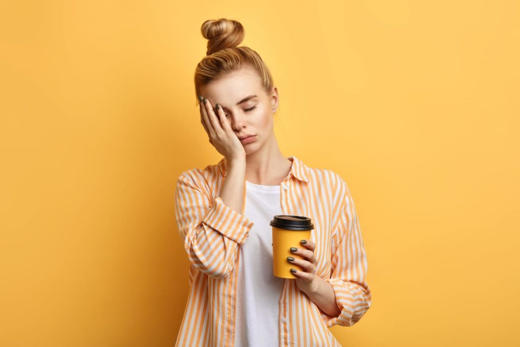 woman looking tired, holding a cup of coffee