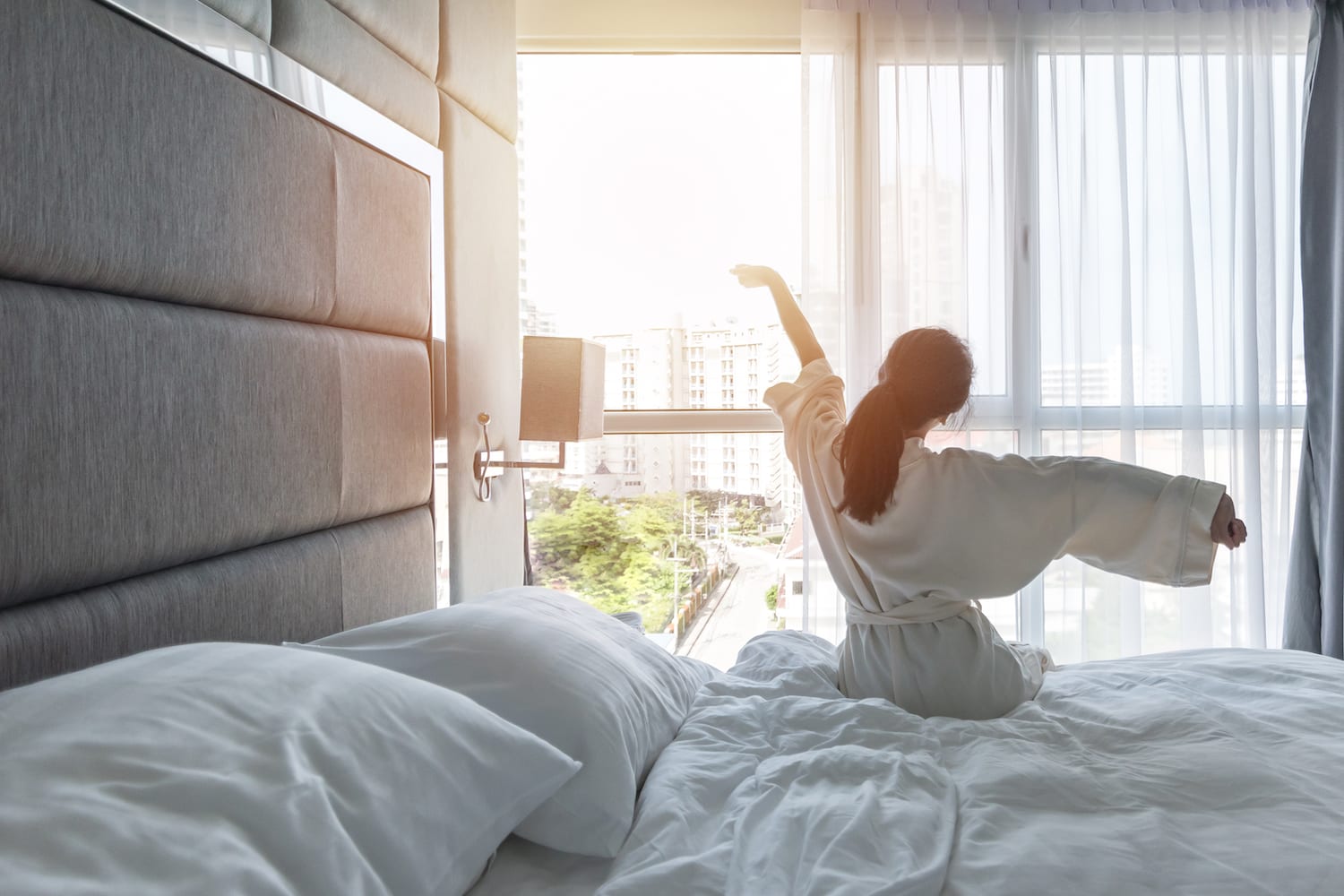 A woman waking up after a sound sleep and looking outside the window