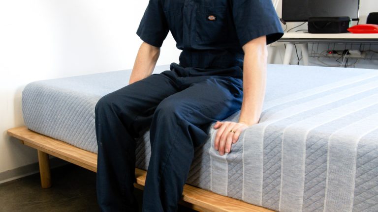 Sleep Foundation tester sitting on the edge of the Leesa Studio mattress to evaluate edge support