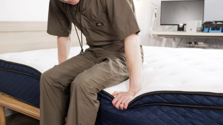 Sleep Foundation tester sitting on the Silk & Snow Hybrid mattress to evaluate edge support