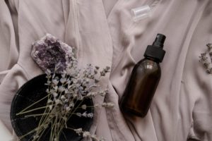 Glass bottle on mauve sheets with lavender and an amethyst geod