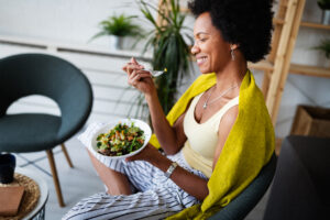 A cheerful woman eating a fresh vegetable salad at home.