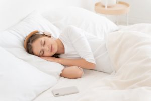 Woman in bed listening to ASMR with headphones