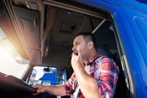 A tired truck driver yawns in the drivers seat