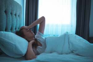 A young woman lying in bed at night, wide awake with a headache.