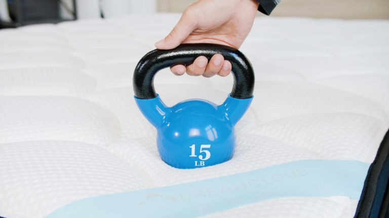 Sleep Foundation tester pressing a 15-pound kettlebell into the DreamCloud mattress