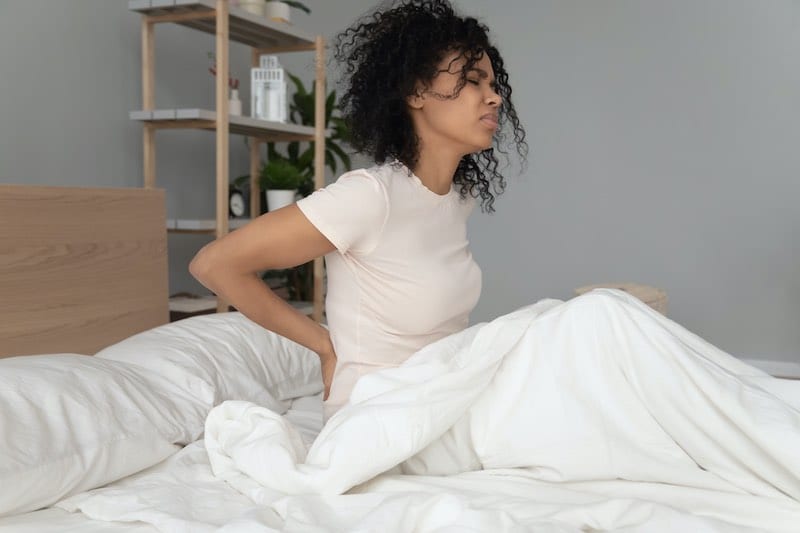 Woman sitting up in bed rubbing her sore back