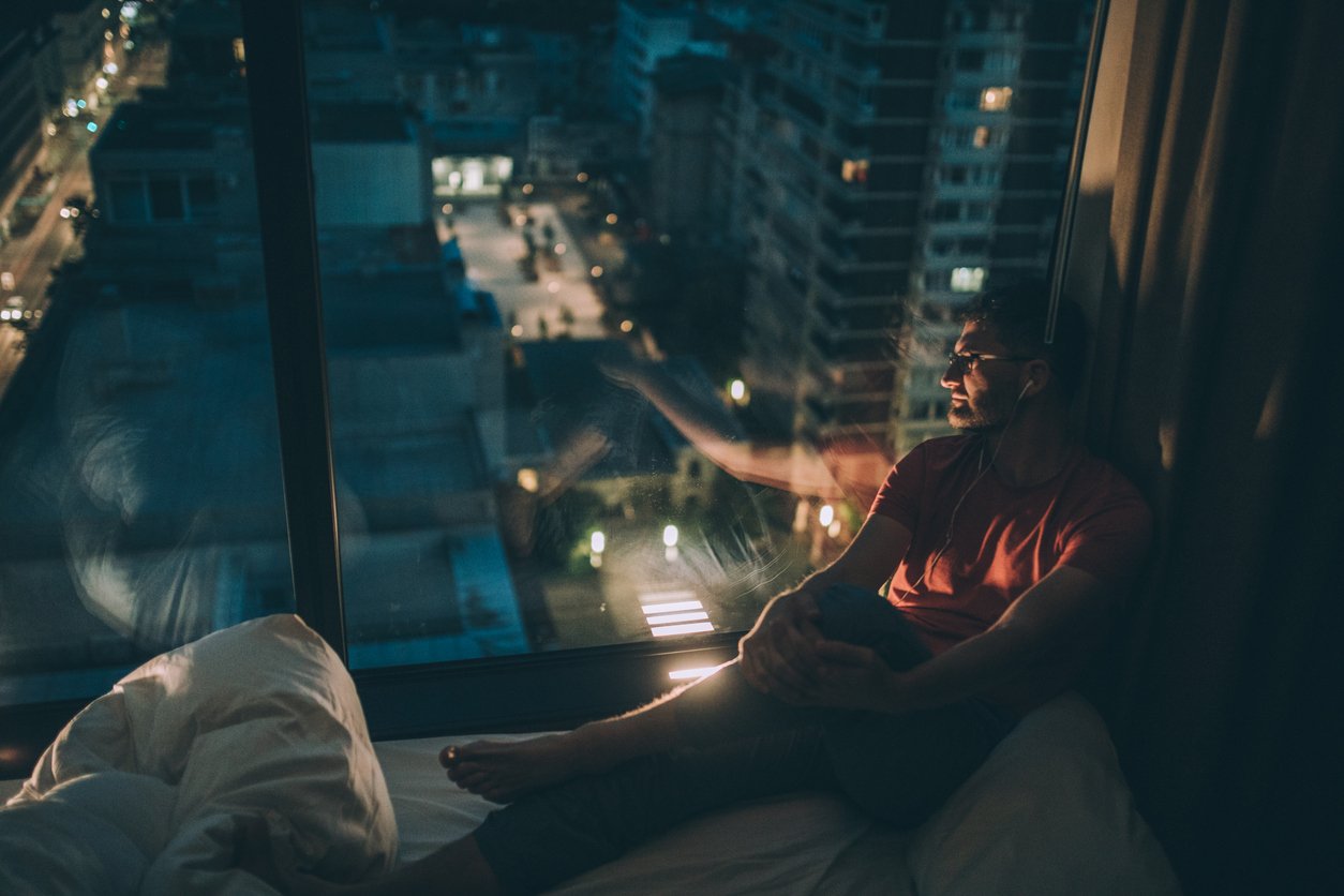 Man sitting in the bedroom with headphones and looking through window Image