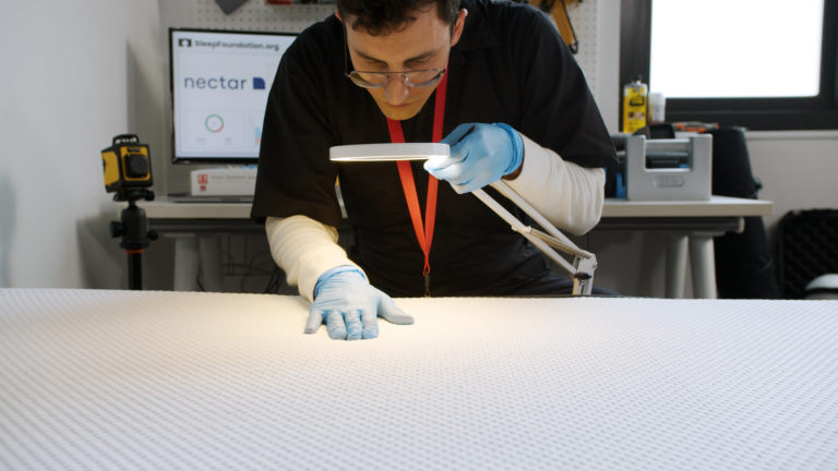Sleep Foundation tester inspecting the Nectar Premier mattress surface with a magnifying lamp