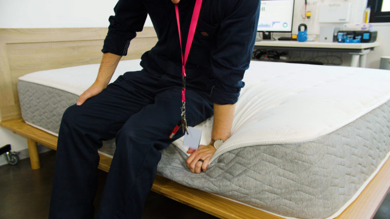 Sleep Foundation tester sitting on the Allswell Luxe Hybrid mattress to evaluate edge support