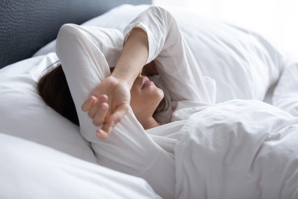 Why You Keep Having Recurring Dreams Woman waking up after bad dream, covering eyes