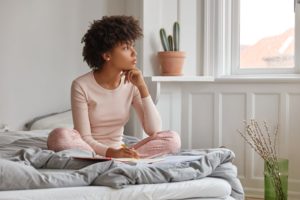 Woman writing in journal while in bed wearing pajamas