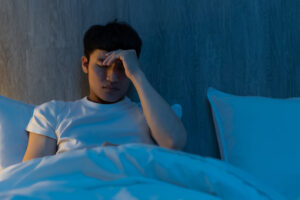 Worried man sitting up in bed at night while holding his head.