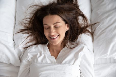Woman lying on back in bed happy