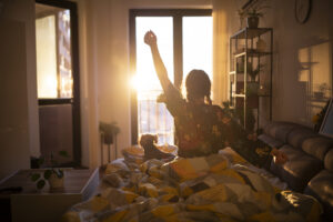 Young woman streching in bed in the morning while looking at the sunrise.