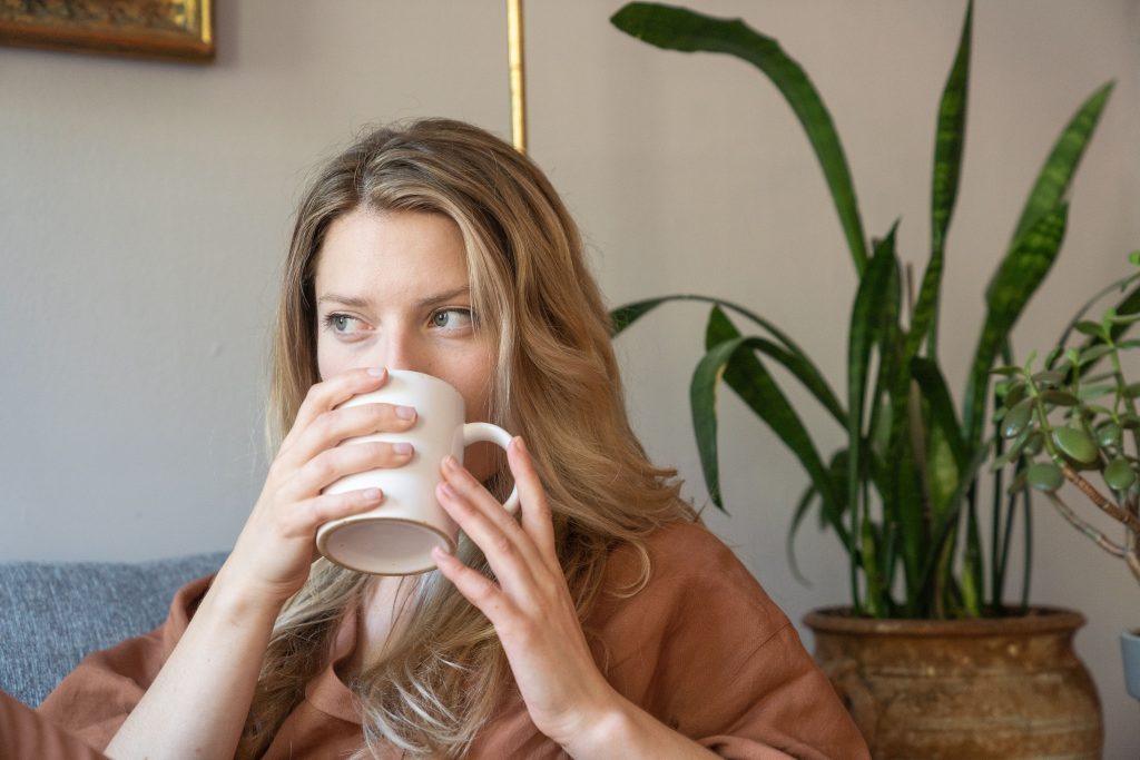 A woman enjoys a peaceful moment sipping warm milk at home, surrounded by indoor plants