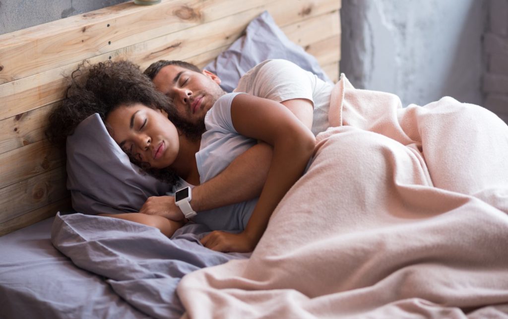 stock image of a couple lying in bed together beneath a pink blanket