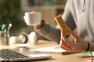 A person holds a hot beverage and a granola bar